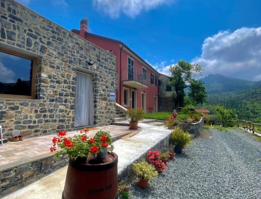Agriturismo Torsivì vista esterna: edificio in pietra e intonaco rosa, decorato con fiori e barili di legno, immerso nel paesaggio collinare.
