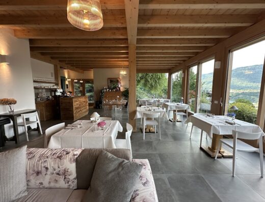 Sala da pranzo luminosa all'Agriturismo Verdecrudo con tavoli imbanditi, sedie bianche, ampie finestre con vista sulla natura e soffitto in legno.
