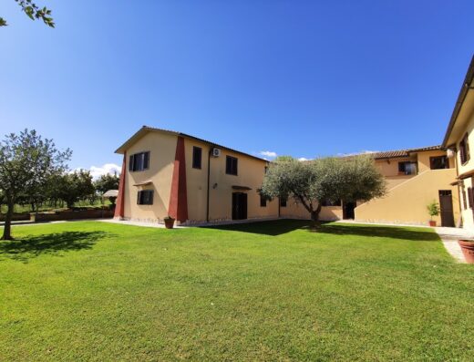 Agriturismo Zugarelli: Veduta esterna della struttura con prato verde, edifici color crema e cielo azzurro. Ideale per un soggiorno rilassante.