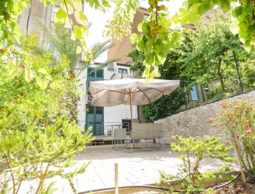 Patio esterno di Al Qatta B&B, con ombrellone, tavolo e sedie circondati da vegetazione lussureggiante. Ideale per relax e vacanze.