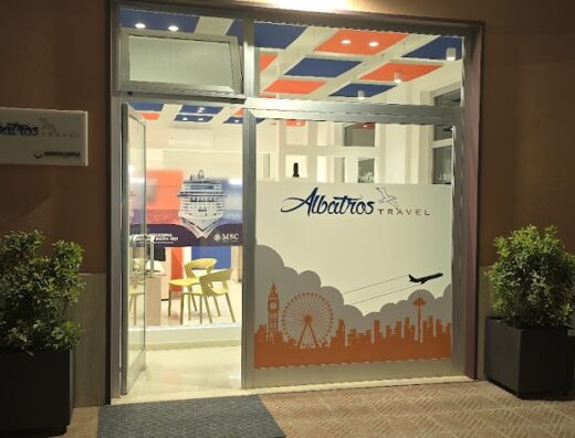 Ingresso dell'agenzia viaggi Albatros Travel con decorazioni a tema viaggio, tra cui una nave da crociera MSC e skyline di città famose.