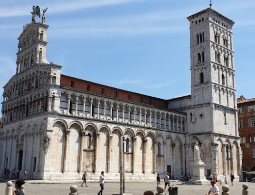 La facciata romanica della Chiesa di San Michele in Foro a Lucca, con la sua imponente loggia e la statua dell'Arcangelo Michele in cima, vista dalla piazza.