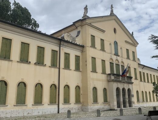 Albergo Ducale, un edificio storico con persiane verdi chiuse, balcone con bandiere e statue sul tetto a Sabbioneta, Italia.