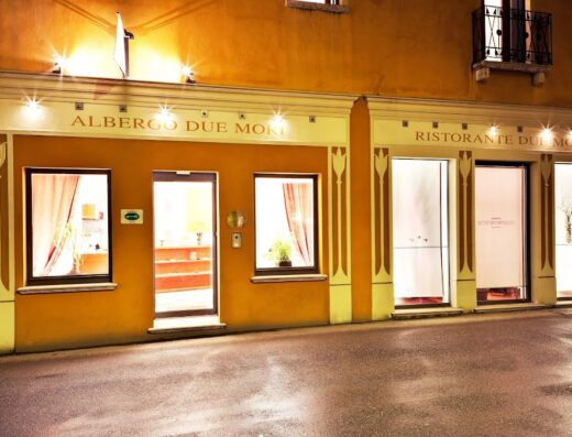 L'Albergo Due Mori e il Ristorante del Mori illuminati di sera, con le vetrine e l'ingresso visibili dalla strada.