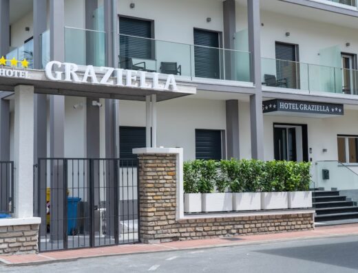 Ingresso dell'Albergo Graziella ad Arma di Taggia, con insegna luminosa, cancellata in ferro battuto e dettagli architettonici moderni. Ideale per vacanze e soggiorni.