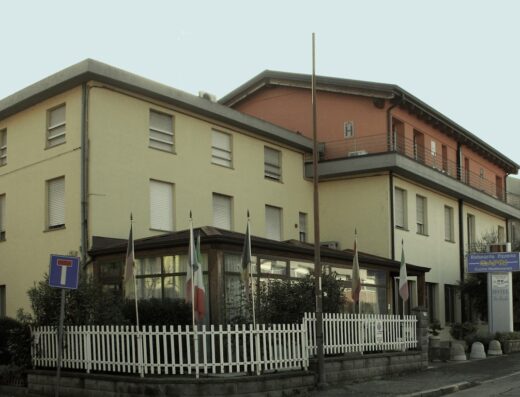 Albergo La Rosta: Esterno dell'hotel con bandiere italiane, insegna del ristorante pizzeria Capri, recinzione bianca e cartello stradale. Ideale per viaggi e soggiorni.