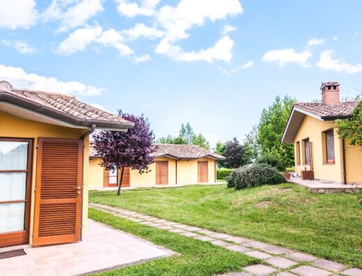 Albergo Le Macerine view of yellow bungalows with tiled roofs and brown wooden doors surrounded by green lawns and trees under a blue sky