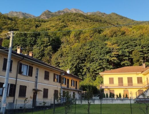 Albergo L'Ostu Del Povr-om: View of the charming Italian hotel nestled against a backdrop of lush green mountains and trees under a clear blue sky.