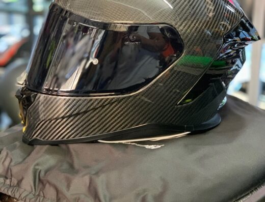 Casco da moto in fibra di carbonio ALEXBOX17, con visiera scura, poggiato su una sacca protettiva nera. Accessorio per motociclisti.