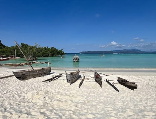 Barche tradizionali malgasce in legno sulla spiaggia di sabbia bianca di Nosy Iranja, Madagascar, con mare turchese e cielo azzurro. Servizi turistici e marketplace di viaggi ad Allasca.