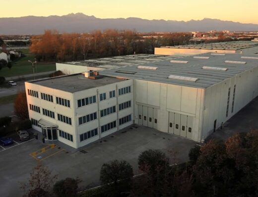 Veduta aerea dello stabilimento ALTUR S.R.L., azienda specializzata in soluzioni per il settore motociclistico e dei trasporti, con parcheggio antistante e montagne sullo sfondo.