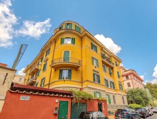 Andenis Tiber House, un edificio giallo a Roma con persiane verdi, balconi in ferro battuto e cielo azzurro sullo sfondo.