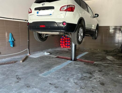 Auto bianca sollevata su un ponte di sollevamento presso AngEli Autolavaggio, che offre servizi di cura e manutenzione auto.