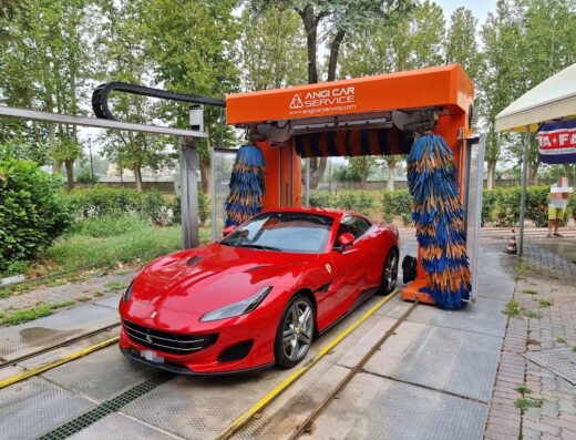 Una Ferrari rossa in un autolavaggio Angi Car Service ad Alessandria, con spazzole blu e gialle pronte a pulire la carrozzeria.