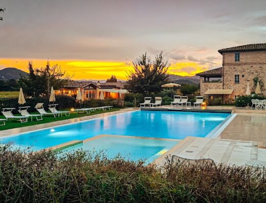 Tramonto pittoresco sulla piscina dell'Anna Boccali Resort, con lettini prendisole e architettura toscana sullo sfondo.