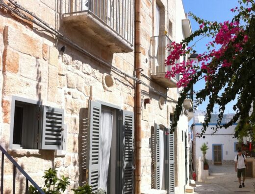 Charming stone facade of Antico Mondo Rooms & Suites, featuring balconies, shuttered windows, and flowering bougainvillea for a delightful travel experience.