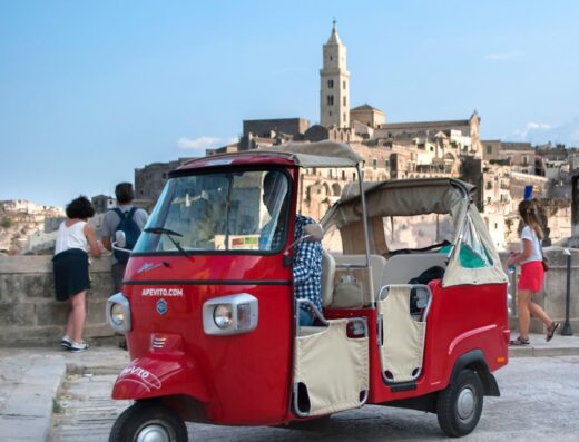 Tour Ape Vito a Matera: caratteristico motocarro rosso Ape Calessino parcheggiato con vista panoramica sui Sassi di Matera, patrimonio UNESCO.