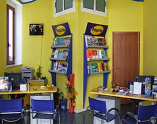 Interno dell'agenzia viaggi e tour operator Appuntamento Viaggi, con scaffali di offerte viaggio, scrivanie e sedie blu.