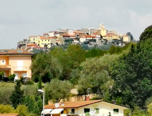 Paesaggio italiano con vista di un borgo collinare, case colorate con tetti rossi, immerso nel verde. Perfetto per un viaggio in moto alla scoperta di Arcobaleno.
