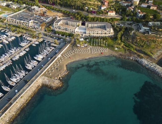 Vista aerea dell'Aregai Marina Hotel & Residence con la marina piena di barche a vela, la spiaggia privata e l'architettura moderna dell'hotel.