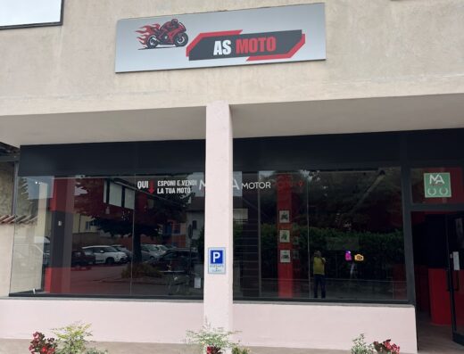 Facciata del negozio AS Moto, rivenditore di moto e accessori. Insegna con logo moto fiammante, vetrine con esposizione e vendita moto, piante decorative.