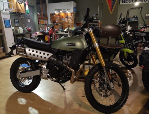 Motocicletta Caballero verde oliva esposta presso Motomeccanica Milano, officina specializzata in aste e bilancieri. Dettaglio degli pneumatici tassellati e scarico a fori.