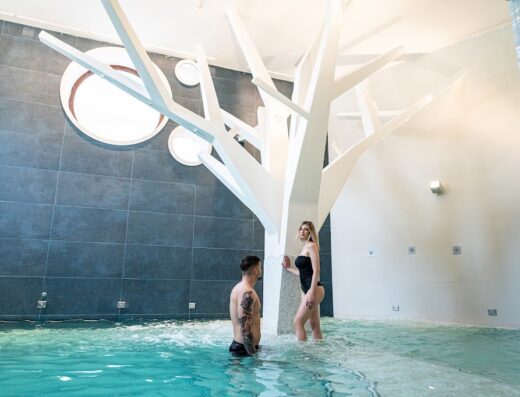 A couple enjoying the Astrea Wellness & Spa, standing in a pool with a decorative white tree-like structure, showcasing the spa's luxurious amenities and relaxation services.