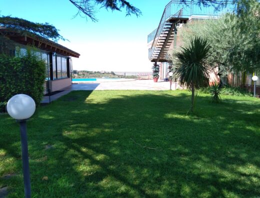 Aura Club Valle degli Ulivi: Vista del giardino con prato verde, piscina in lontananza e struttura con scale esterne.