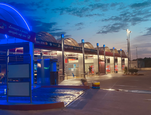 Auto Brill lavaggio self service con illuminazione al neon blu, postazioni di lavaggio auto e piazzale esterno.