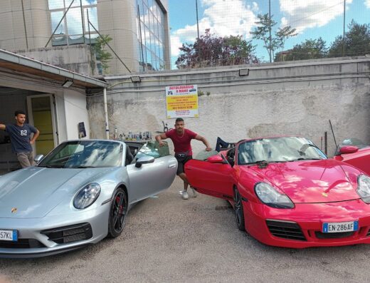 Auto lavaggio egiziano: due addetti posano tra una Porsche 911 GTS argento e una Porsche Boxster rossa con portiere aperte.