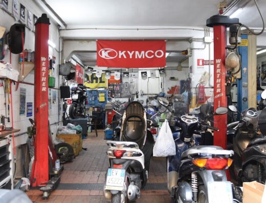 Interno dell'officina SR Motors a Napoli, specializzata in riparazione moto e scooter, con diverse moto parcheggiate, ponte sollevatore e insegna Kymco.