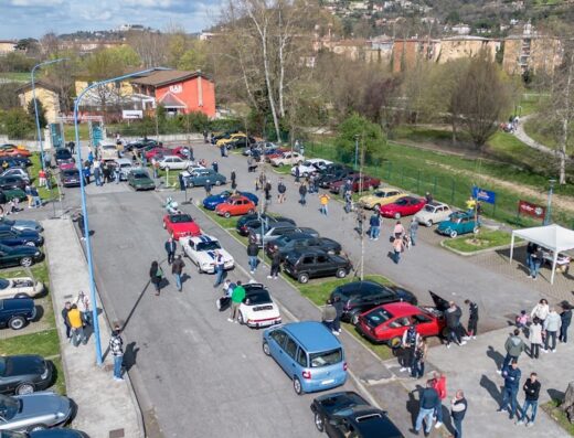 Raduno di auto storiche a Brescia: vista aerea di un parcheggio affollato di auto d'epoca, con appassionati e curiosi che le ammirano.