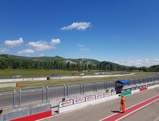 Autodromo Riccardo Paletti, Varano de' Melegari: Vista della pista con auto da corsa, protezioni di sicurezza e paesaggio collinare sullo sfondo.