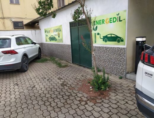Immagine di autofficina con colonnine di ricarica per auto elettriche e cartelli pubblicitari per la ricarica di veicoli elettrici.