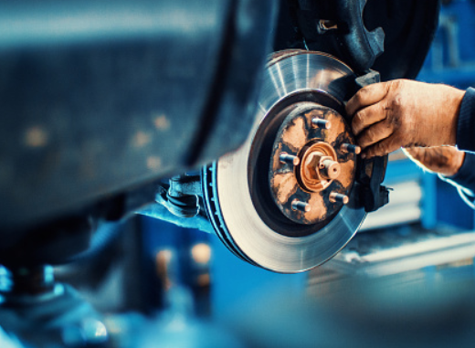 Primo piano dei freni di una moto in riparazione presso l'Autofficina Bortolotti, con un meccanico che lavora sul disco freno.