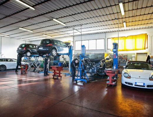 Interno dell'Autofficina dalla Valle con auto su ponte sollevatore e meccanici al lavoro su diverse vetture.