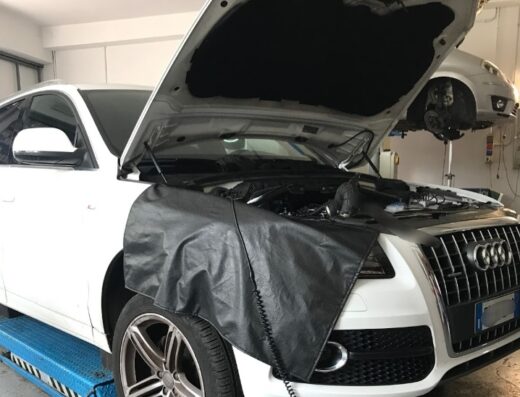 Auto bianca in riparazione presso l'Autofficina di Girolamo Lorenzo, con cofano motore aperto e protezione in pelle nera. Servizio di manutenzione auto.