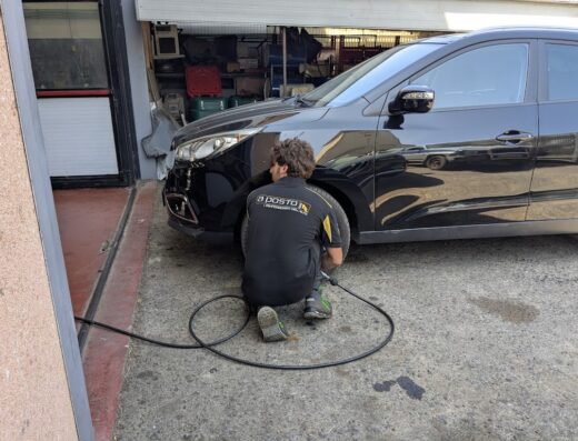 Un meccanico al lavoro su un'auto nera presso Autofficina LC Service, focalizzato sulla riparazione e manutenzione auto.