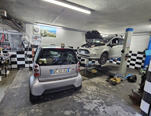 Interno dell'Autofficina Meccanica Di Martino con una Smart Fortwo parcheggiata e un'auto su un ponte sollevatore per riparazioni meccaniche.