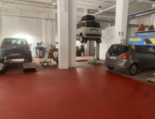 Interno dell'Autofficina Pisino con tre auto in riparazione: una Golf su ponte, una Multipla sollevata e una monovolume grigia.