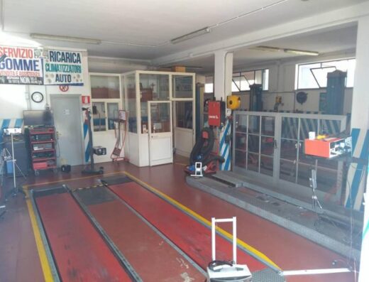 Interno dell'Autofficina Valloreo con ponte sollevatore, attrezzature per la riparazione auto e cartelli che indicano i servizi offerti.