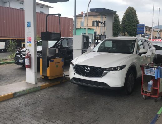 Autolavaggi Stella: Una Mazda bianca e altre auto in fila per il lavaggio auto, con un carrello di accessori per la pulizia visibile.
