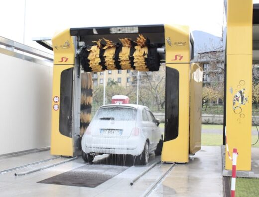 Autolavaggio automatico Aquarama S7: un'auto bianca è in fase di lavaggio con spazzole rotanti e schiuma, servizio di pulizia veicoli