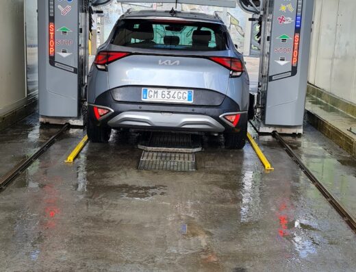 Autolavaggio automatico Istobal: SUV grigio Kia Sportage in fase di lavaggio, vista posteriore con spazzole in azione per pulizia auto.