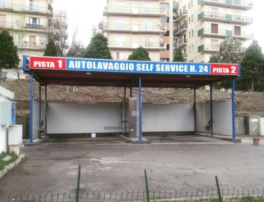 Autolavaggio self-service con due piste dedicate al lavaggio moto e altri veicoli, situato in area urbana con edifici residenziali.