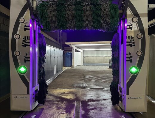 Autolavaggio automatico WashTec pronto per lavare una moto, con indicazione 'Posizionare Veicolo' e luci al neon viola.