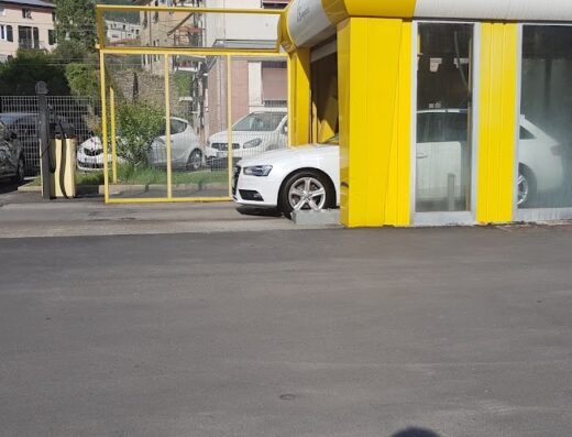 Autolavaggio automatico: Una vettura bianca viene lavata all'interno di una struttura gialla e bianca, con altre auto parcheggiate nelle vicinanze.