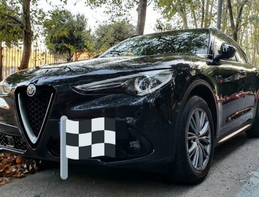 Alfa Romeo Stelvio nera parcheggiata su strada con una bandiera a scacchi davanti al paraurti, contesto di autolavaggio 2 Fratelli