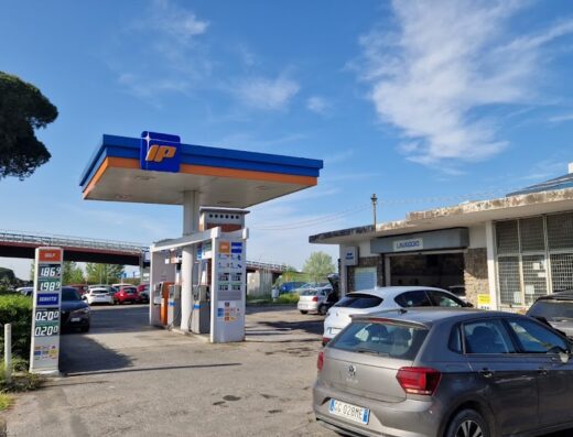 Autolavaggio a mano presso stazione di servizio IP: auto in fila per il lavaggio auto self-service, prezzi carburante visibili.