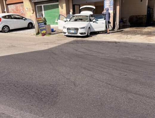 Autolavaggio a mano: un uomo lava una Audi bianca con portiere e bagagliaio aperti. Servizio professionale per la cura dell'auto.